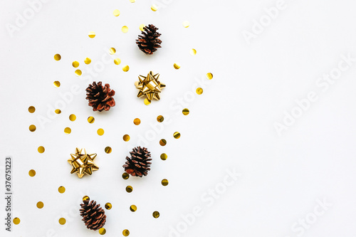 Festive golden bows and cones on a white background with confetti. Christmas or New Year background. Nearby copy space or space for text.