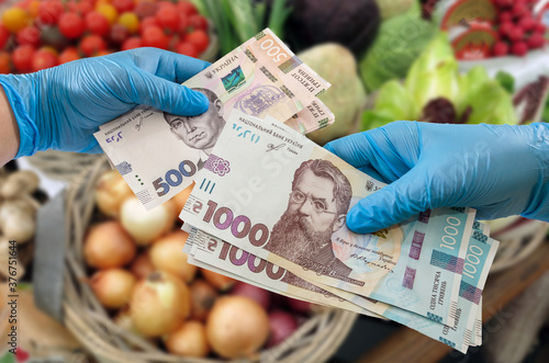 shopper in gloves with hryvnia on the background of vegetables in the supermarket. Close-up. Coronavirus protection concept