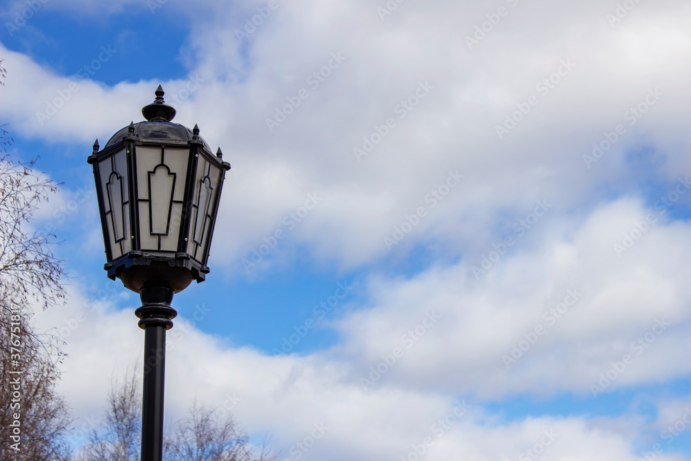Vintage street lamp with patterns on a blue sky background with clouds