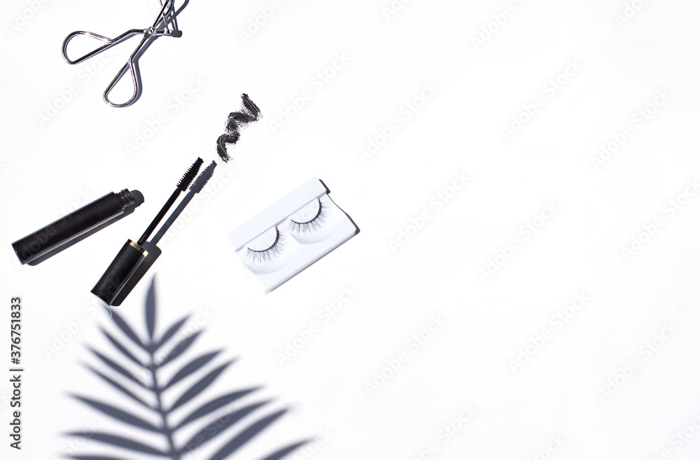 Black mascara frame with brush smear, an eyelash curler and false eyelashes on the bright white background. Cosmetic isolated products. Copy space Black mascara frame with brush smear, an eyelash curler and false eyelashes on the bright white background. Cosmetic isolated products. Copy space