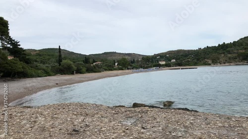 Agioi Anargyroi beach, with its grey pebbles and turquoise sea and umbrellas with tourists in Spetses island in Greece