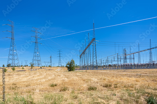 View of high voltage power plant and high voltage cable crossing towers in green grass field