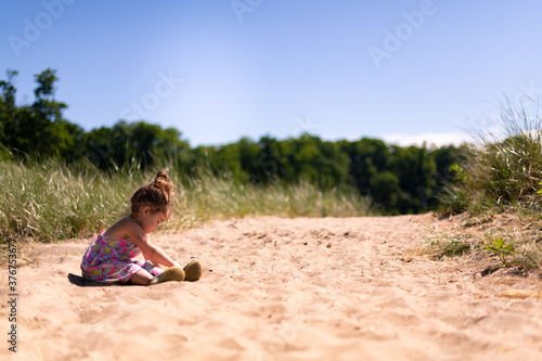 A toddler girl sitting in the sand and playing