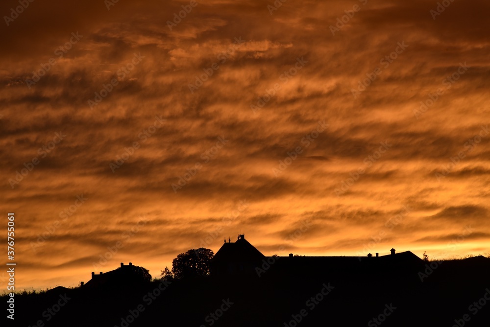 Dramatic colorful clouds at sunset, with a silhouette of a human dwelling. 08-22-2020, Middle Bohemia, Czech Republic.