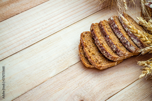 Bakery products. Rye bakery with crusty loaves and crumbs. Fresh loaf of rustic traditional bread with wheat grain ear or spike plant on natural wooden background. Concept - Cooking at Home.