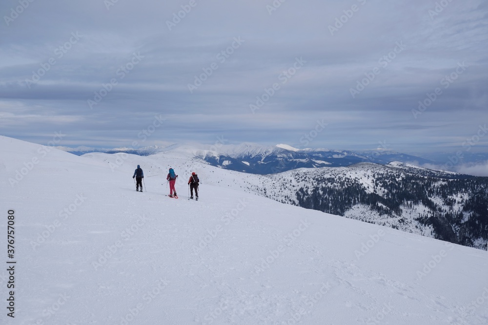Beautiful winter mountain views during a snowshoe hike along the red ridge trail towards Velka Chochula Peak in the Low Tatras, Slovakia - silhouettes of tourists on trail