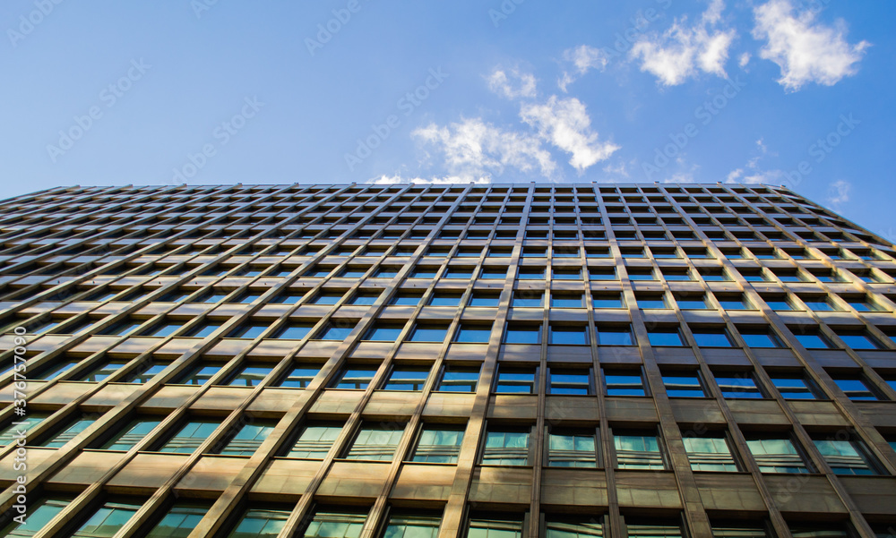 Bottom-up view of a glass modern office building, against a blue sky with clouds