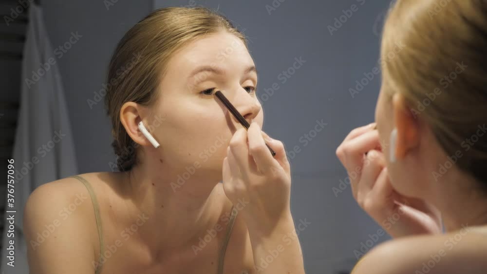 Attractive woman putting on makeup with brush adding mascara on eye. European girl at bathroom tide up at the evenig Attractive woman putting on makeup with brush adding mascara on eye. European girl at bathroom tide up at the evenig
