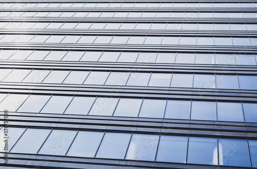 Endless rows of identical gray Windows of a modern glass office building-a skyscraper which reflects the blue sky and white clouds