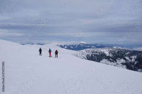 Beautiful winter mountain views during a snowshoe hike along the red ridge trail towards Velka Chochula Peak in the Low Tatras, Slovakia - silhouettes of tourists on trail © Iwona