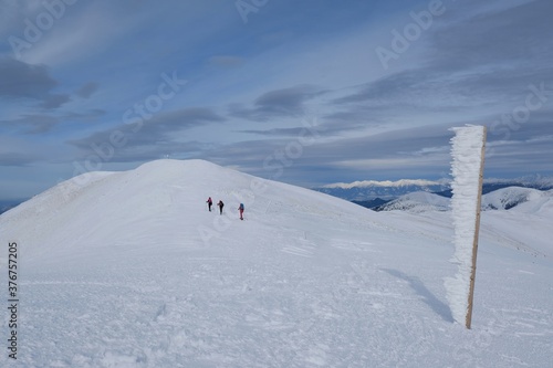 Beautiful winter mountain views during a snowshoe hike along the red ridge trail towards Velka Chochula Peak in the Low Tatras, Slovakia - frozen pole and silhouette of tourists © Iwona