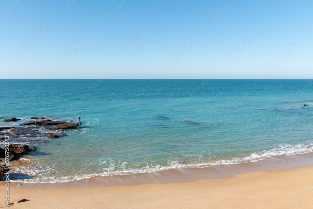 Paisaje rocoso y un hombre pescando en las rocas, en la playa de Cabo de Roche o Calas de Roche, ubicada en Conil de la Frontera, en la provincia de Cádiz, España.