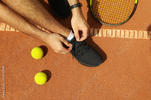 Man ties his shoelaces on clay court with racket and balls © Atlas