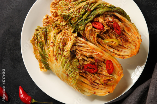 The Korean national cuisine. Peking cabbage kimchi with vegetables, red sauce and chili pepper on a white plate on a black background. Flatlay, horizontal. Background image, copy space