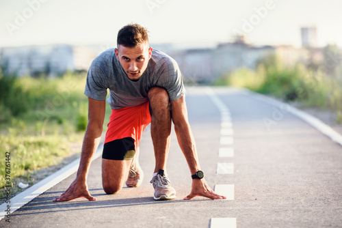 Sports man runner with smart watch in start position preparing to run