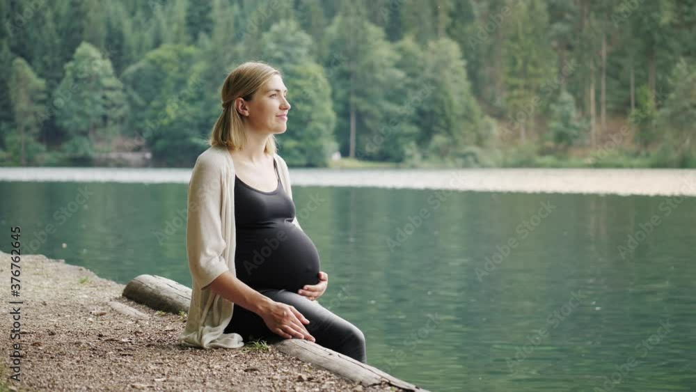 Pregnant woman touching gently her tummy when sitting near the mountain lake. Pregnant woman touching gently her tummy when sitting near the mountain lake.