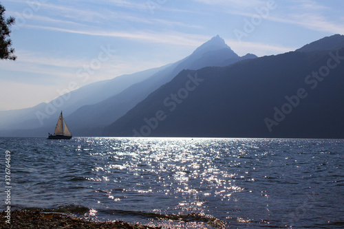 sailing boat on blue water with sun reflection with panoramic view of apls mountain lake