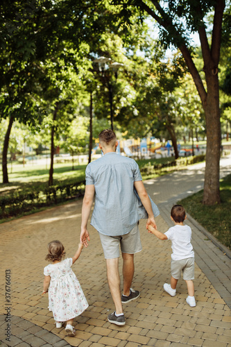Loving dad with little kids walking at the park, caring father hold children hands, lovely man spend time with toddlers, enjoy family weekend outdoors, parenthood concept