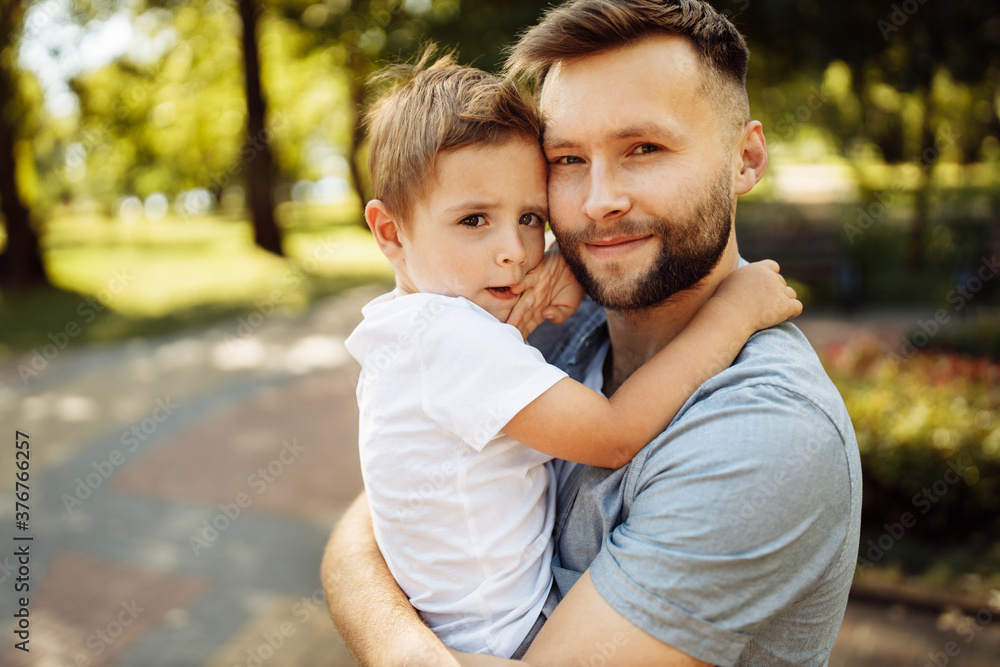 Portrait of handsome man with little boy at the park, lovely son sitting on fathers arms, smiling, dad and toddler spend time together, enjoy tender family moments, parenthood concept Portrait of handsome man with little boy at the park, lovely son sitting on fathers arms, smiling, dad and toddler spend time together, enjoy tender family moments, parenthood concept