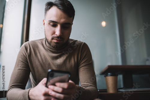 Calm man messaging on smartphone in cafeteria