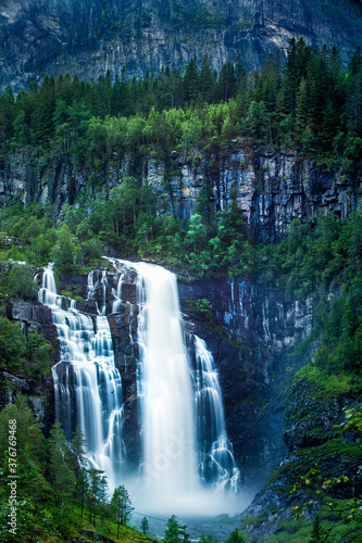 Skjervsfossen waterfall surrounded by pine forest and huge cliffs, near Voss, Norway photo