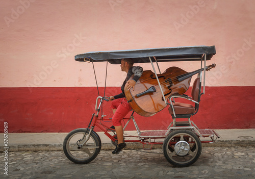 Man carrying double bass on tricycle in colonial street, Trinidad de Cuba