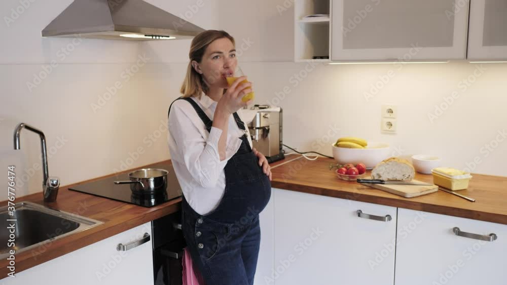 Pregnant girl drinks juice in the kitchen. Pregnant girl drinks juice in the kitchen.