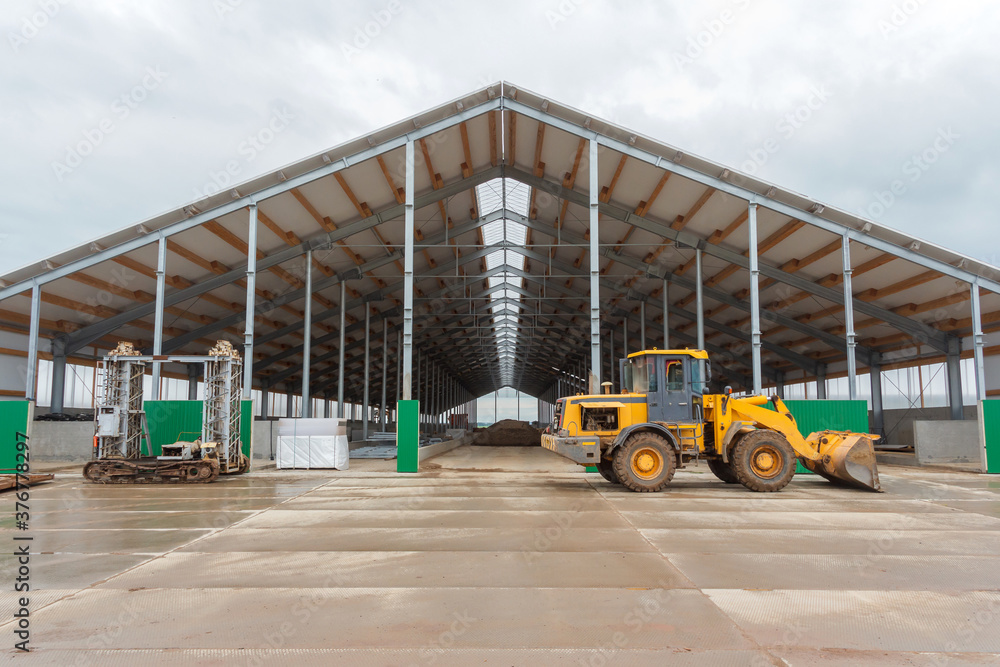 Metal frame of the building with a sandwich panel of insulation on the wall and construction machinery. Construction machinery on the background of a building under construction Metal frame of the building with a sandwich panel of insulation on the wall and construction machinery. Construction machinery on the background of a building under construction