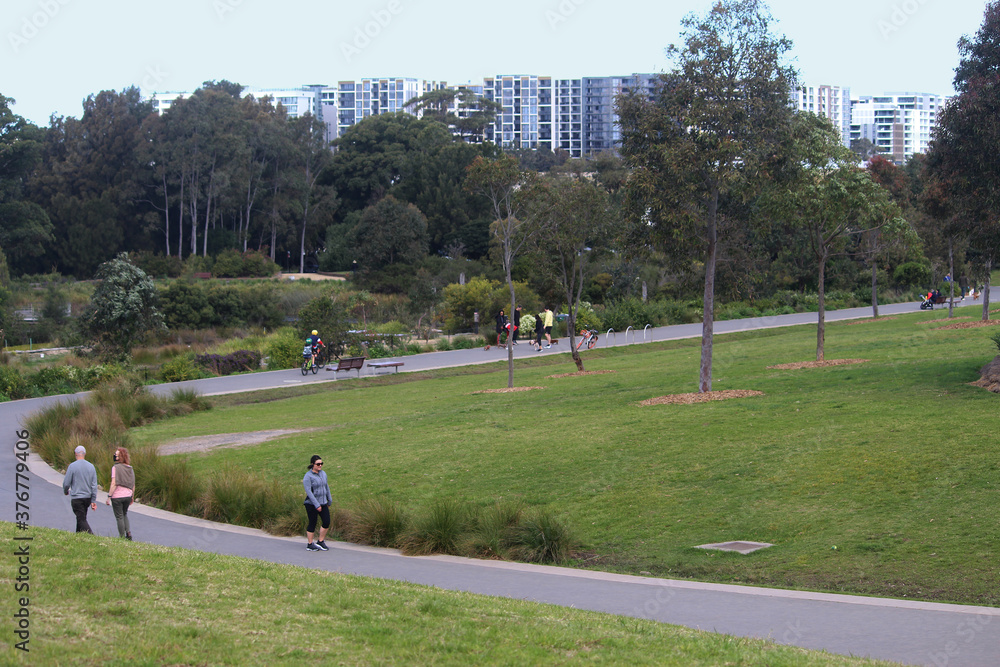 Obraz premium Sydney, NSW / Australia - August 23 2020: People walking along a meandering path at Sydney Park with trees and apartment buildings in the background