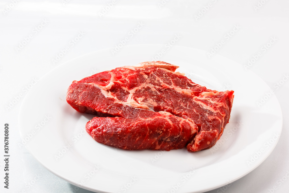 Raw marbled beef steak sits on a white plate Raw marbled beef steak sits on a white plate