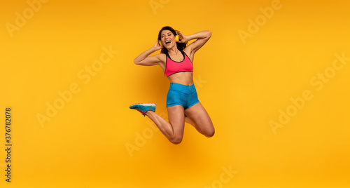 Fototapeta Naklejka Na Ścianę i Meble -  Sport woman jumps on a yellow background and listen to music. Happy and joyful expression.