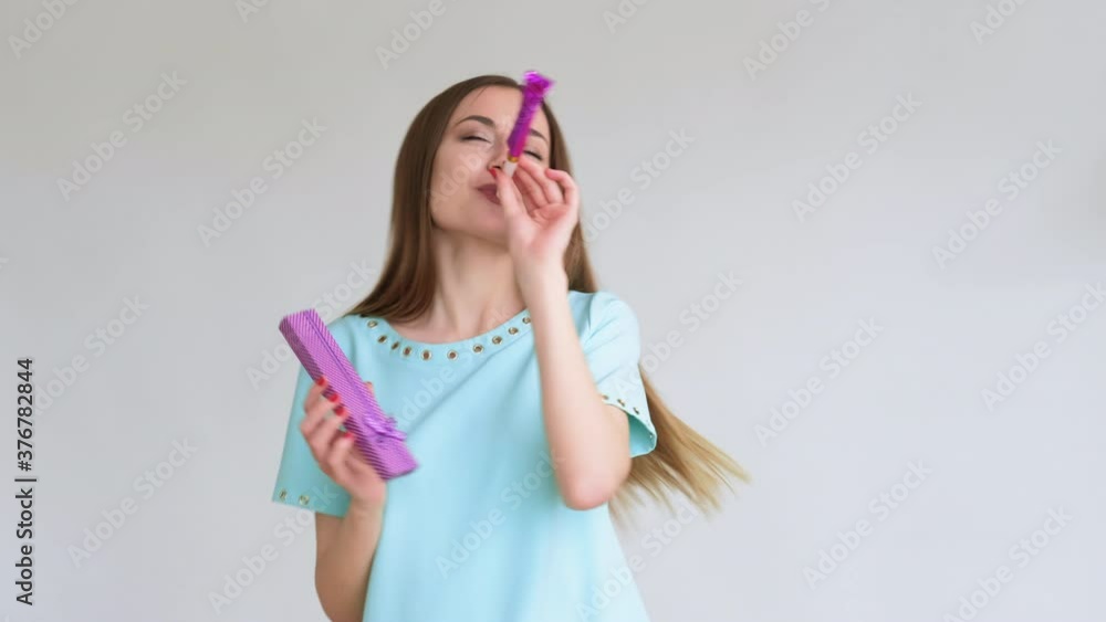 Birthday celebration. Special day. Portrait of happy amused woman in blue dancing alone with jewelry box smiling blowing horn isolated on light background. Gift delivery New normal. Birthday celebration. Special day. Portrait of happy amused woman in blue dancing alone with jewelry box smiling blowing horn isolated on light background. Gift delivery New normal.