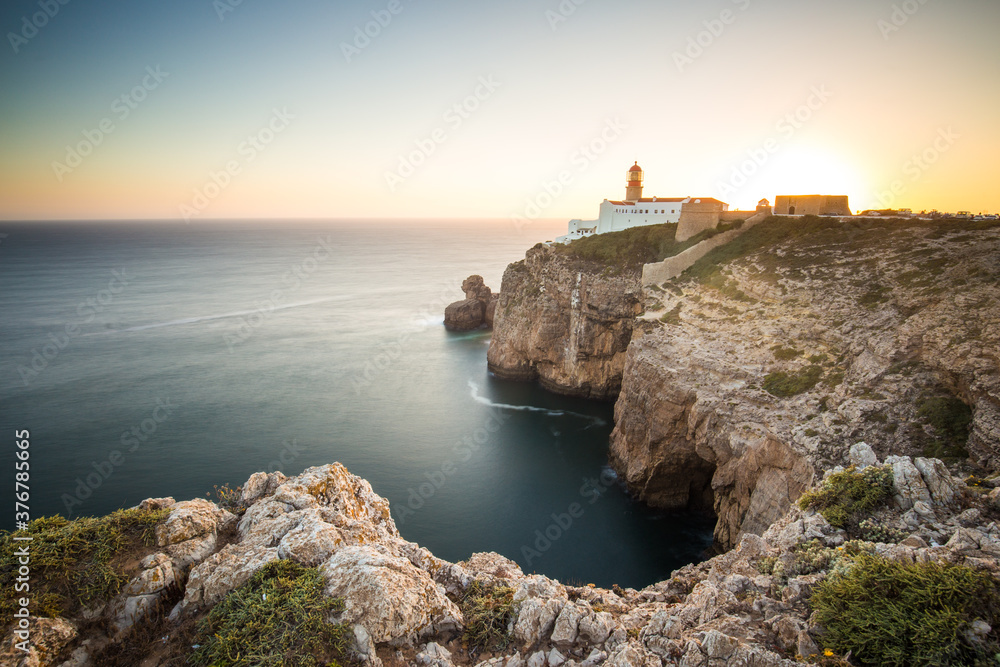 View of lighthouse on rocky coastline by sea