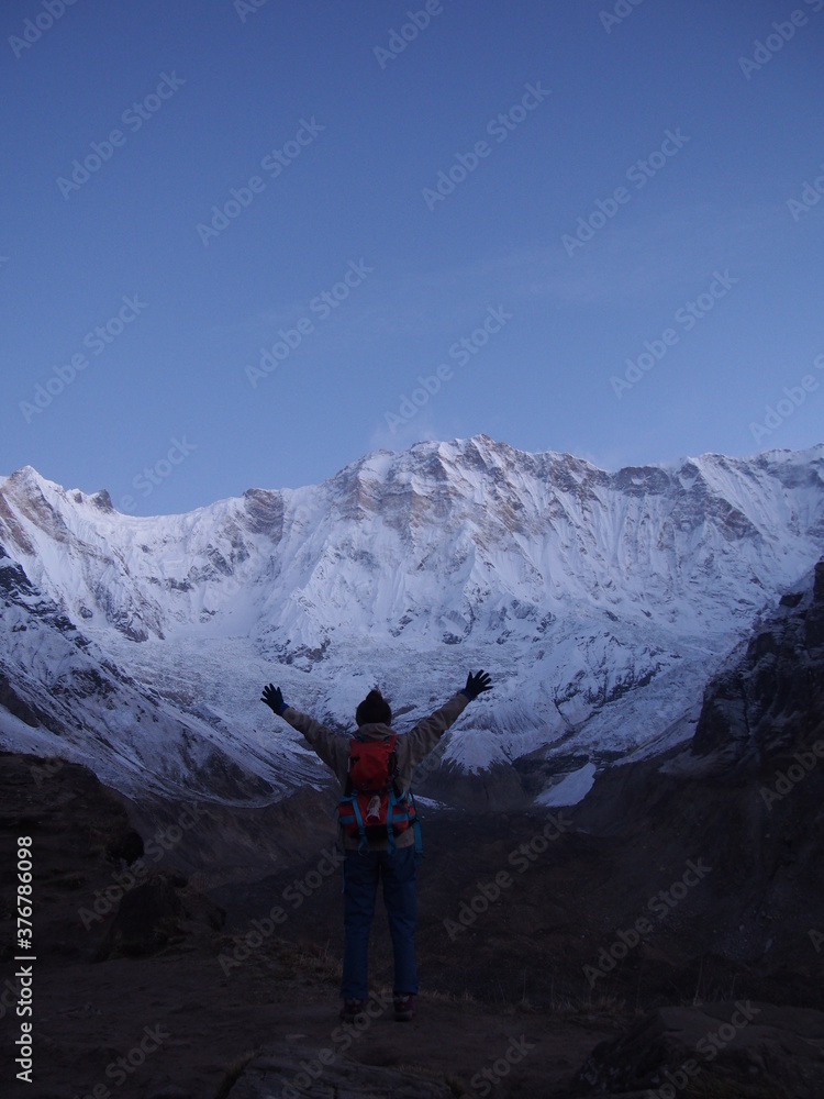 A climber raises her arms in front of a snow-covered rock in the early morning, ABC (Annapurna Base Camp) Trek, Annapurna, Nepal