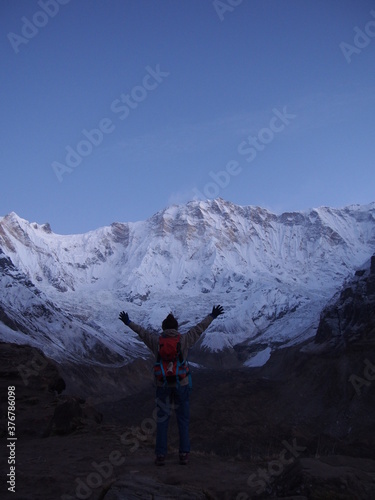 A climber raises her arms in front of a snow-covered rock in the early morning, ABC (Annapurna Base Camp) Trek, Annapurna, Nepal