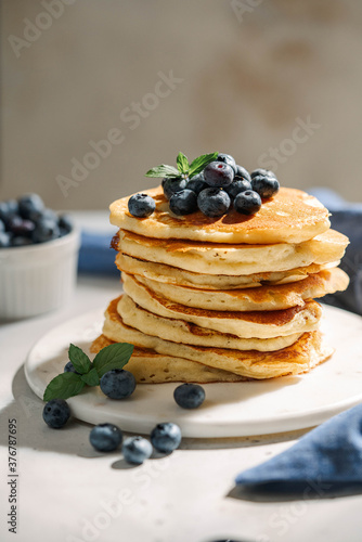 Homemade pancakes, fresh blueberries with maple syrup on white table. Healthy American breakfast or brunch, favorite meal.