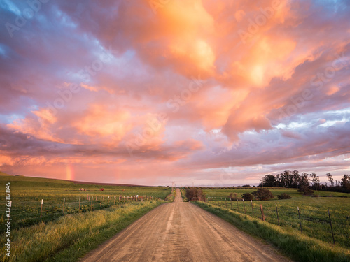 View of dirt road passing through fields during sunset