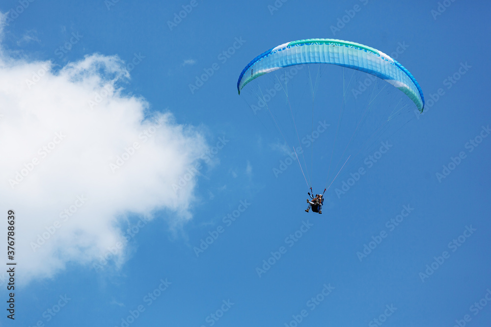 Blue Paraglider flying into the sky with clouds on a sunny day Blue Paraglider flying into the sky with clouds on a sunny day