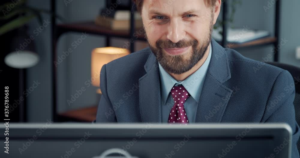 Successful businessman looking at computer screen and feeling happiness. Smiling bearded man in formal clothing working at office center. Successful businessman looking at computer screen and feeling happiness. Smiling bearded man in formal clothing working at office center.
