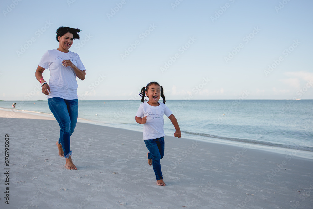 Fototapeta premium Mom and daughter on the beach running around and having fun stock photo royalty free