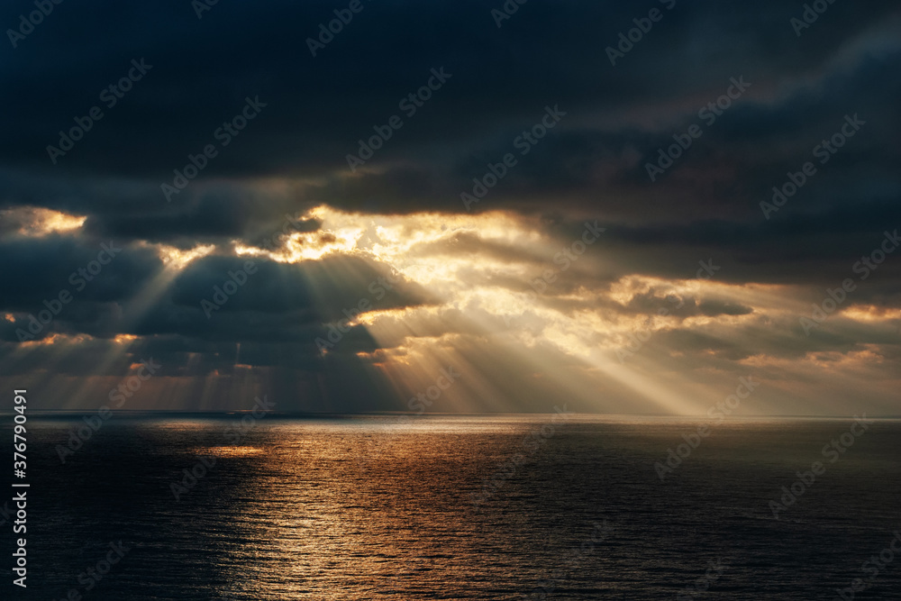Orange sunset with sun rays through dark clouds over the sea with reflection Orange sunset with sun rays through dark clouds over the sea with reflection