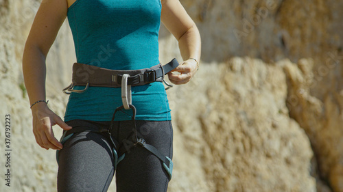 CLOSE UP Female rock climber tightens the harness around her waist before ascent