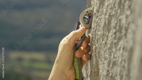 Photography CLOSE UP: Rock climber clips a carabiner into a bolt screwed into the cliff