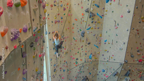 DRONE: Fit young woman scales a challenging route in an indoor climbing center.