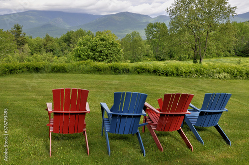 Colorful red and blue lawn chairs offering tourists a relaxing hillside view of Cannon Mountain and Mount Lafayette in New Hampshire's Franconia Notch State Park.