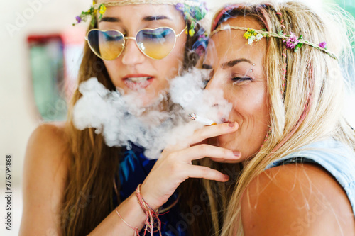 Two women sisters or friends sharing a smoke or joint having fun in summer day - close up real people leisure activity unhealthy living concept