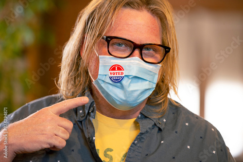 Caucasian man wearing mask pointing at an I Voted Today sticker on the mask photo