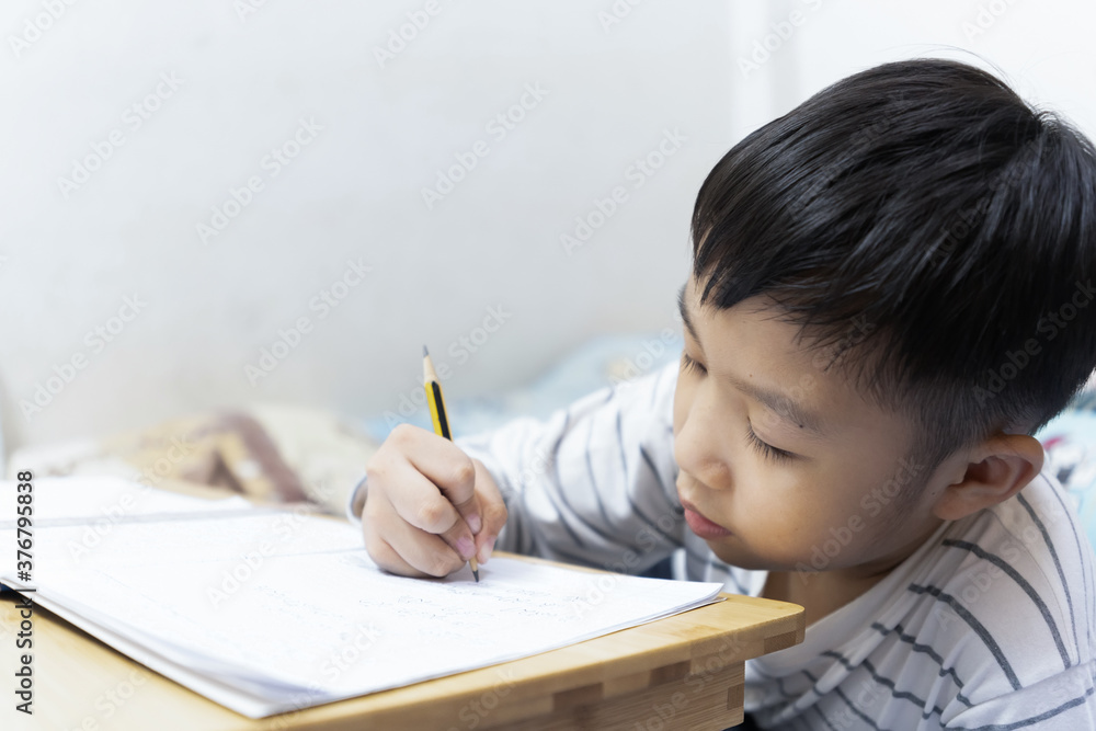Home school and new normal lifestyle concepts.Asian boy studying through online media and do homework at home due to social distance policy to prevent the spread of the coronavirus(Covid-19) Home school and new normal lifestyle concepts.Asian boy studying through online media and do homework at home due to social distance policy to prevent the spread of the coronavirus(Covid-19)