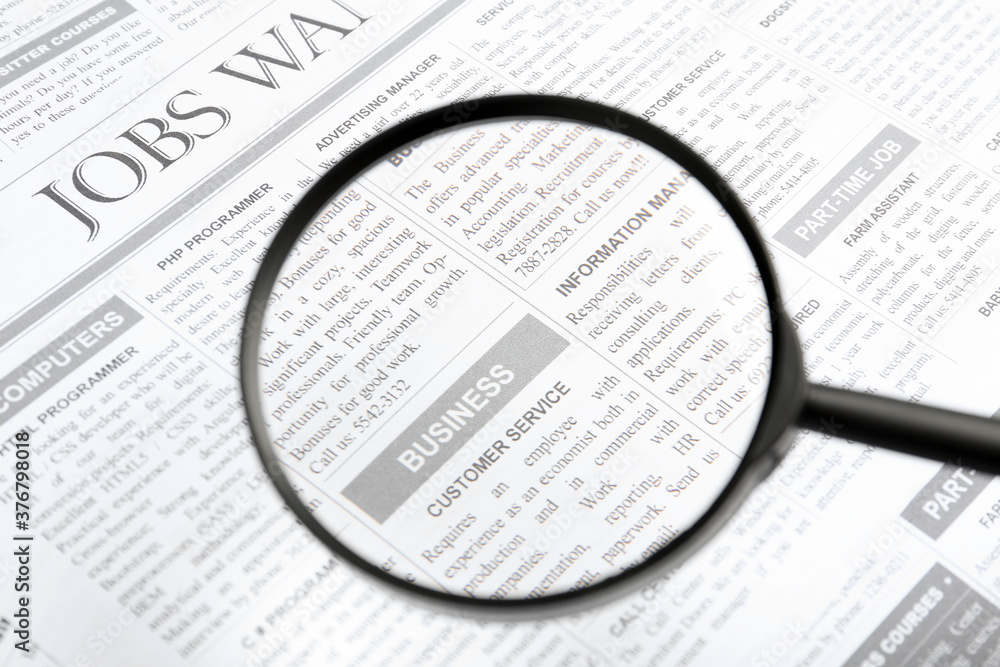 Looking through magnifying glass at newspaper, closeup. Job search concept Looking through magnifying glass at newspaper, closeup. Job search concept