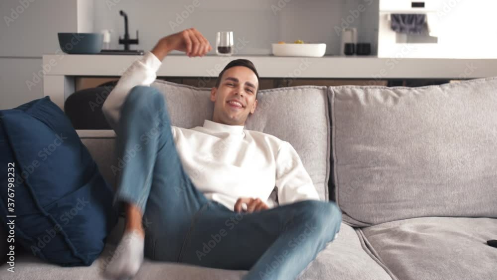 Tired young caucasian man sits on sofa in living room after exhausting work. 4k slow motion footage. Tired young caucasian man sits on sofa in living room after exhausting work. 4k slow motion footage.